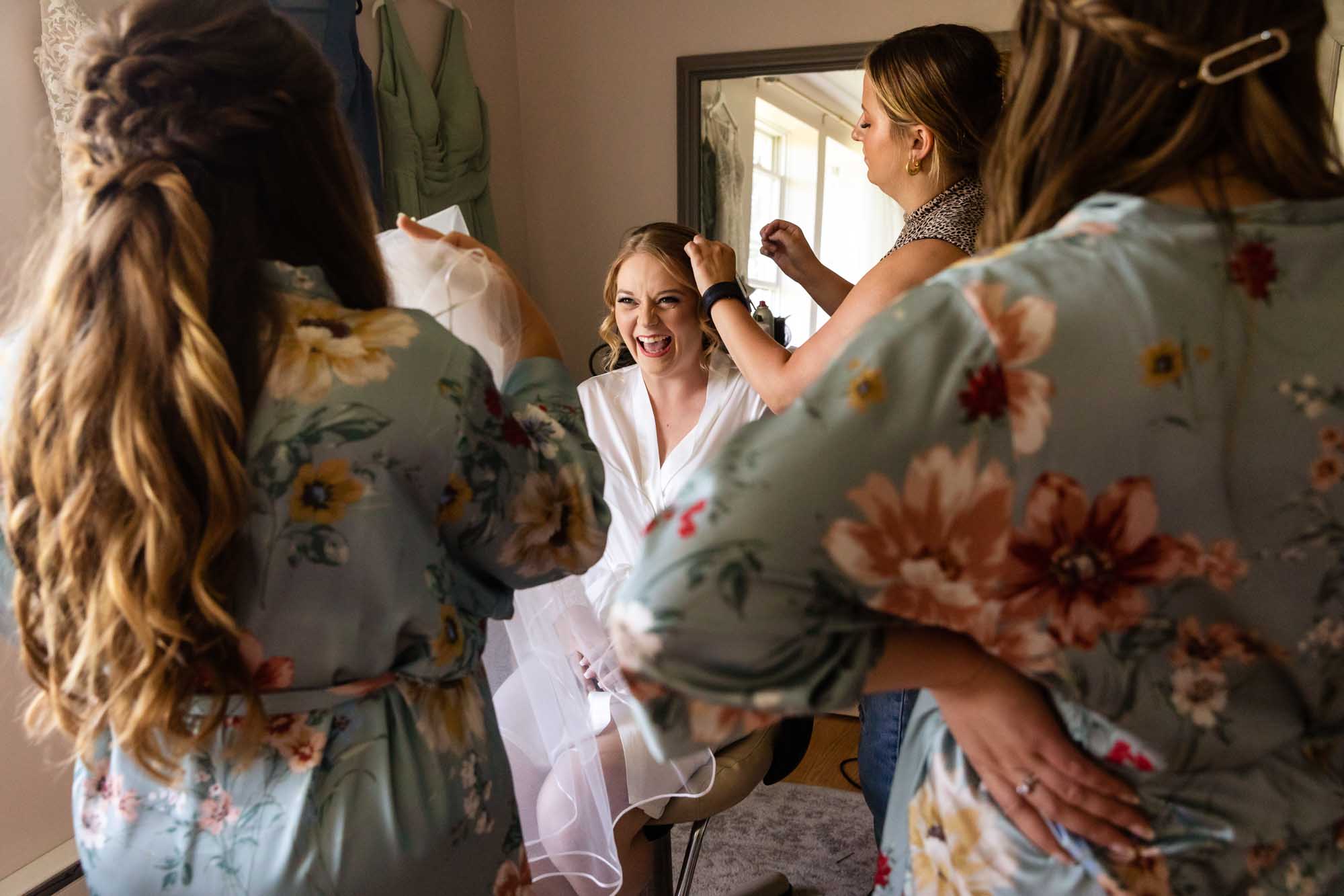 bride laughing, surrounded by her bridesmaids as she gets ready for her wedding at pinehall at eisler farms